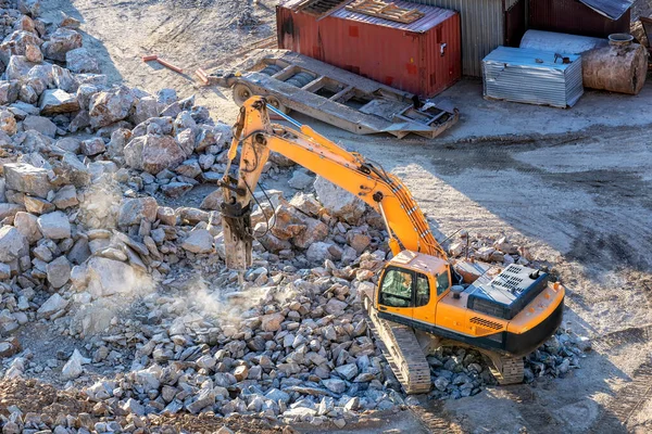 A hydraulic breaker is mounted on the excavator. It is powered by an auxiliary hydraulic system from the excavator, which is fitted with a foot-operated valve for this purpose.