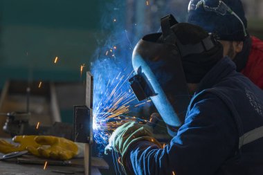 Kaynakçı atölyede gaz metal kaynaklı yapısal bir çelik kaynak yapıyor..