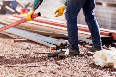 İşçi inşaat alanında metal profilleri kesiyor. Çok yönlü mekanik ve tasarım özellikleri nedeniyle metal profil sayfaları çatı ve çatı kaplaması, dış duvarlar ve duvar kaplaması ve ayrıca zemin olarak kullanılabilir.
