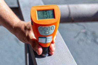 Boya müfettişi kum püskürtücü maddenin yüzey pürüzünü ölçüm cihazıyla kontrol ediyor..