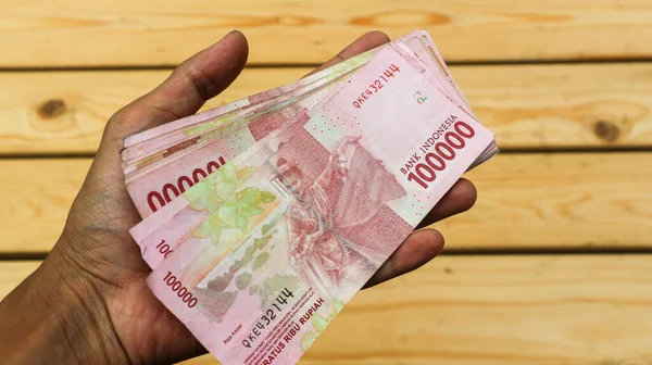 stock image A man's hand holds a hundred thousand rupiah note.