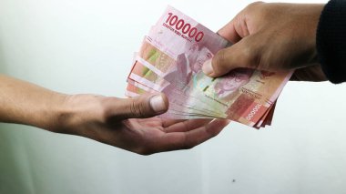 Siyah paltolu Asyalı genç bir kadın sadece erkeklerle rupiah ticareti yapıyor. İşlem konsepti, finansal konsept. Asyalı adam Rupiah banknotlarını tutuyor, siyah beyaz arka planda izole edilmiş..