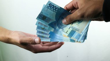 Siyah paltolu Asyalı genç bir kadın sadece erkeklerle rupiah ticareti yapıyor. İşlem konsepti, finansal konsept. Asyalı adam Rupiah banknotlarını tutuyor, siyah beyaz arka planda izole edilmiş..