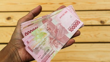 Bir adamın eli yüz bin rupiah tutar. Siyah paltolu Asyalı genç bir kadın rupiah 'ı erkeklerle sadece eller, işlem konsepti, finansal konsept ile takas ediyor..