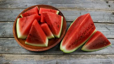 Ahşap tabakta kırmızı karpuz dilimleri ve gri tahta arka planda izole edilmiş. Sağlıklı yemek, vejetaryen. Antioksidan