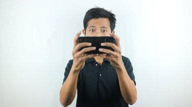 Ciddi bir ifadesi olan Asyalı adam cep telefonuyla oyun oynuyor..