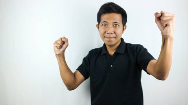 Genç Asyalı adam gülümsüyor ve yumruğunu sıkıyor. Beyaz stüdyo arka planında izole edilmiş, seçici odaklı.