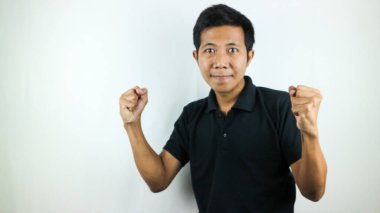 Genç Asyalı adam gülümsüyor ve yumruğunu sıkıyor. Beyaz stüdyo arka planında izole edilmiş, seçici odaklı.