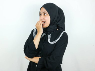 Rüya gibi gülümseyen Asyalı Müslüman kadın parmağını ısırıyor ve yan tarafa bakıyor, düşünüyor ya da ilginç bir fikir üretiyor, güzel bir şeyin hayalini kuruyor, beyaz arka planda duruyor.