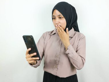 Akıllı bir telefon ekranına bakarken tesettürlü genç bir Asyalı kadının şaşırmış ifadesi