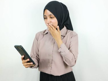 Akıllı bir telefon ekranına bakarken tesettürlü genç bir Asyalı kadının şaşırmış ifadesi