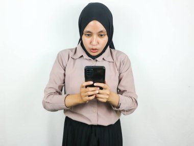 Akıllı bir telefon ekranına bakarken tesettürlü genç bir Asyalı kadının şaşırmış ifadesi