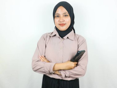 Güzel, genç Asyalı Müslüman kadın, beyaz arka planda izole edilmiş akıllı telefonu tutarak güvenle gülümsüyor. Reklam kavramı.