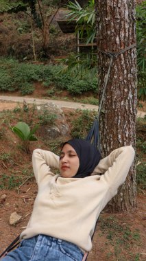 Güneşli yaz öğleden sonrasında terasta hamakta uyuyan türbanlı genç Müslüman kadın..