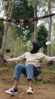 Yeşil bahçedeki hamakta dinlenen türbanlı dalgın, genç bir kadın..