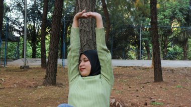 Doğanın tadını çıkarıyorum. Genç Müslüman kadın kollarını kaldırarak yaz yeşil parkında temiz havanın tadını çıkarıyor.