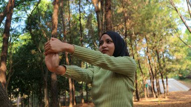 Müslüman kadınlar egzersiz yaparken kollarını uzatıyor ve çam ağaçlarının ortasında temiz hava soluyor. Egzersiz ve Yaşam Tarzı konsepti. Mutlu bir hayat ve sağlık hizmeti teması. Doğa ve Açık hava teması.