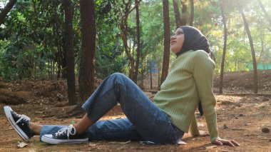 Genç Müslüman kadın kaygısız, güneşli bir günde çimlerde dinleniyor. Kapalı gözlü hippi kadın kahve molası sırasında rahatlığın ve özgürlüğün tadını çıkarıyor..