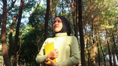 Genç Müslüman Kadın kitabı elinde tutuyor. Sabah güneşinde parkta kitap okumak.