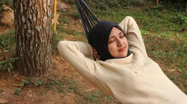 Güneşli yaz öğleden sonrasında terasta hamakta uyuyan türbanlı genç Müslüman kadın..