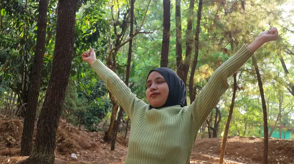 Doğanın tadını çıkarıyorum. Genç Müslüman kadın kollarını kaldırarak yaz yeşil parkında temiz havanın tadını çıkarıyor.