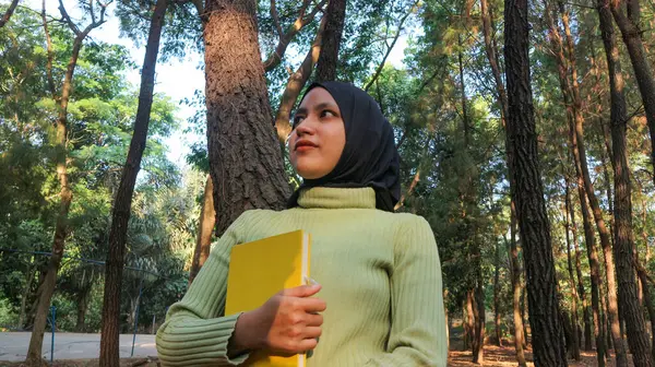 Genç Müslüman Kadın kitabı elinde tutuyor. Sabah güneşinde parkta kitap okumak.