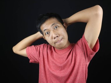 Siyah arka planda elleri başının üzerinde olan Asyalı adamın komik ifadesi.