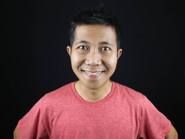 Asyalı adam kameraya bakıp gülümsüyor. Siyah arka planda mutlu bir yüzü var.