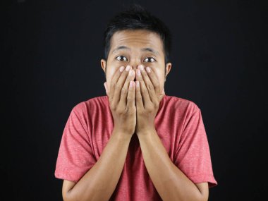 Ağzı kapalı, heyecanlı Asyalı genç adam fotokopi çekilen siyah stüdyo arka planında izole edilmiş.