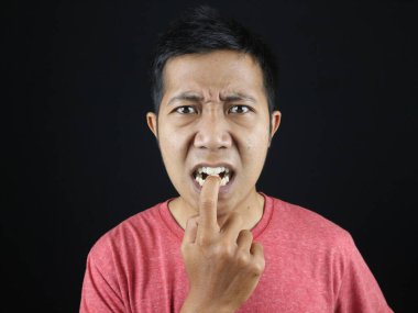 Siyah arka planda izole edilmiş komik yüz ifadesi olan genç Asyalı adam parmaklarını ısırıyor.