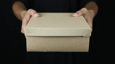 Teslimatçının elleri siyah arka planda karton kutu teslim ediyor. Kargo taşımacılığı, hızlı ulaşım hizmeti, online alışveriş ve lojistik konsept.