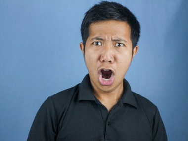 Mavi arka planda yalnız yaşayan Asyalı adamın şok olmuş ve şaşırmış yüzü..