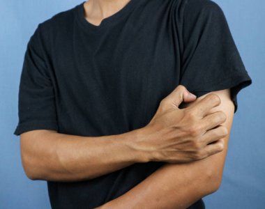 Mavi arka planda elini kaşıyan Asyalı genç adam. Uyuz, mantar enfeksiyonu, egzama, sedef, kızarıklık, alerji gibi kaşındırıcı deri hastalıkları kavramı..