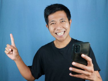 Komik gülümseyen yüz ifadesi. Asyalı adam gülümsüyor. Elinde cep telefonu var.