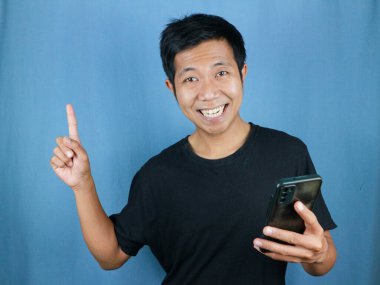 Komik gülümseyen yüz ifadesi. Asyalı adam gülümsüyor. Elinde cep telefonu var.