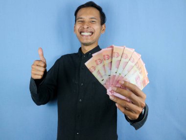 Heyecanlı bir yüz ifadesi. Yakışıklı Asyalı adam, elinde kağıt para banknotları ve iyi niyetli bir jest tutuyor. İş ve finans kavramı.