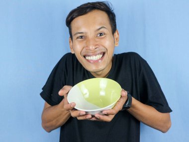 Siyah tişörtlü, Asyalı genç bir adam elinde çanağı gösteren boş bir kâse tutuyor..