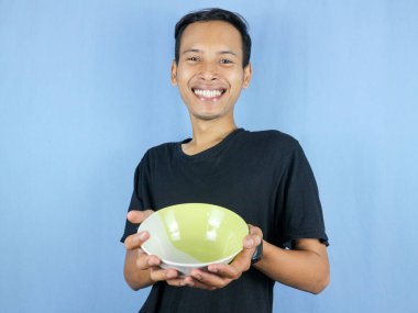 Siyah tişörtlü, Asyalı genç bir adam elinde çanağı gösteren boş bir kâse tutuyor..