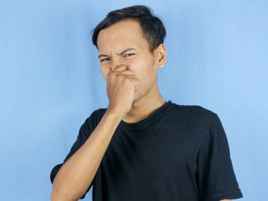 Yakışıklı Asyalı adam pis ve iğrenç bir koku alıyor. Nefesini burnunda tutuyor. Kötü koku konsepti