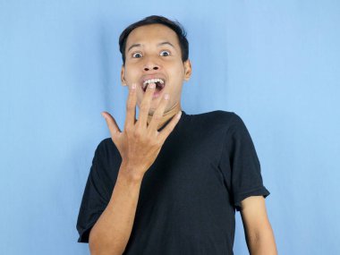 Mavi arka planda yalnız yaşayan Asyalı adamın şok olmuş ve şaşırmış yüzü..