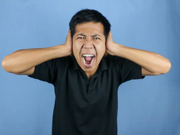 Portrait of funny young Asian man stress or having pain of headache, scream, and cover his ears.