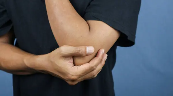 Elbow pain concept : Close up man holding on elbow and feeling a pain. Studio shot isolated on blue background with copy space for text