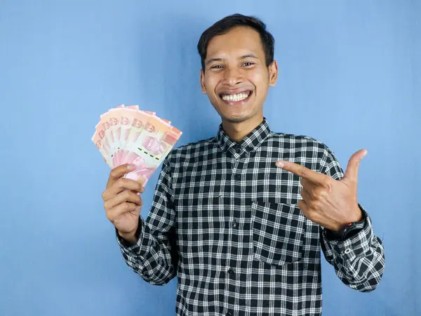 Heyecanlı bir yüz ifadesi. Yakışıklı Asyalı bir adam, bir kenara işaret ederek kağıt para banknotları tutuyor. İş ve finans kavramı.