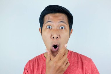 Kırmızı t-shirt giyen Asyalı adamın kameraya bakarken şaşkın ve şaşırmış ifadesi.