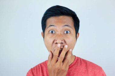 Kırmızı t-shirt giyen Asyalı adamın kameraya bakarken şaşkın ve şaşırmış ifadesi.