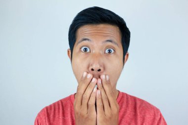 Kırmızı t-shirt giyen Asyalı adamın kameraya bakarken şaşkın ve şaşırmış ifadesi.