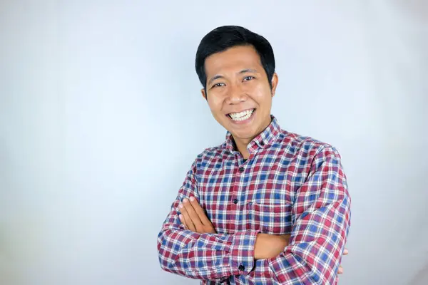 Ekose gömlek giyen genç Asyalı adam kollarını kavuşturup kameraya bakıyor.,