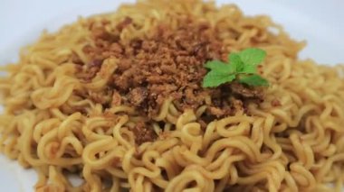 Üzerine baharat ve nane yaprakları serpiştirilmiş, beyaz bir tabakta servis edilen hazır erişteler. Döndürme ekranı