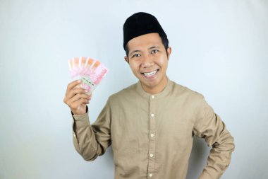 Asyalı Müslüman adamın elinde para tutmasının mutlu ifadesi. Rupiah banknotları beyaz arka planda izole edilmiş.