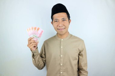 Asyalı Müslüman adamın elinde para tutmasının mutlu ifadesi. Rupiah banknotları beyaz arka planda izole edilmiş.